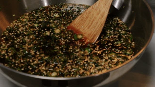 Mixing green chili peppers with soy sauce in a metal bowl using a wooden spatula