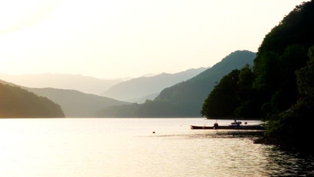 Early morning by a serene lake surrounded by mountains and forests