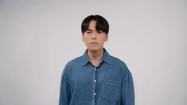 Man in a denim shirt looking straight ahead with a serious expression