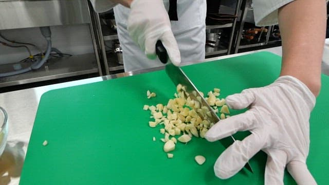 Chef chopping garlic on a green cutting board