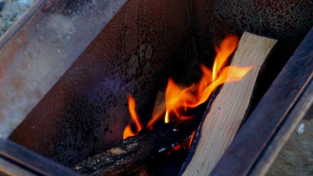 Lighting a fire in an outdoor fire pit with wood and tongs