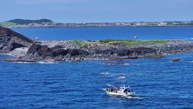 Scenic coastal view of rocky cape and boat passing nearby at sea