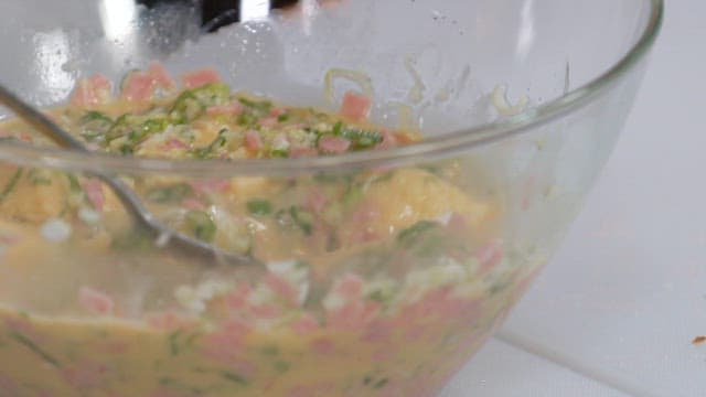 Mixing egg mixture with green onions and bacon and bread in a glass bowl