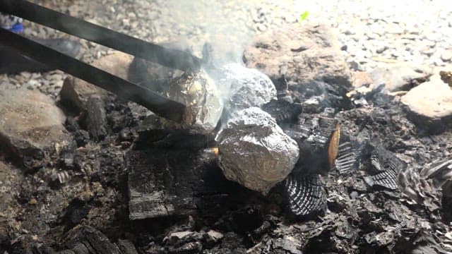 Potatoes wrapped in foil roasting over firewood