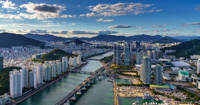 Mountains, rivers, and urban buildings under a blue sky with flowing clouds