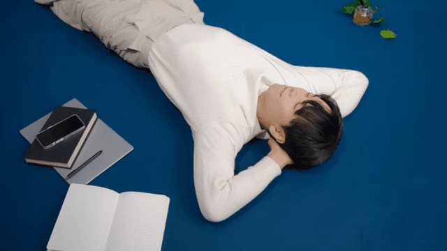 Man lying on the floor with books, notebook, and phone