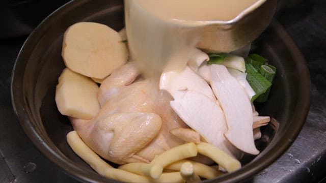 Pouring broth into a pot containing various ingredients