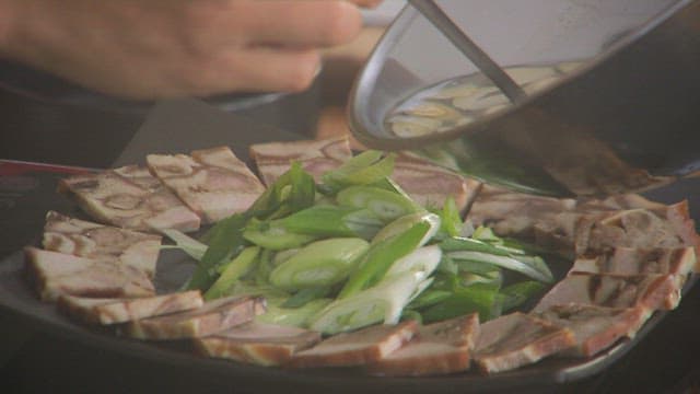 Pouring garlic sauce over the boiled pork with green onions