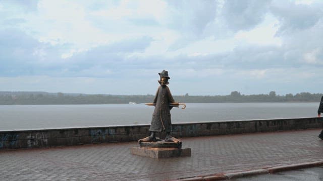 Bronze statue of Anton Chekhov with an umbrella on a riverside promenade