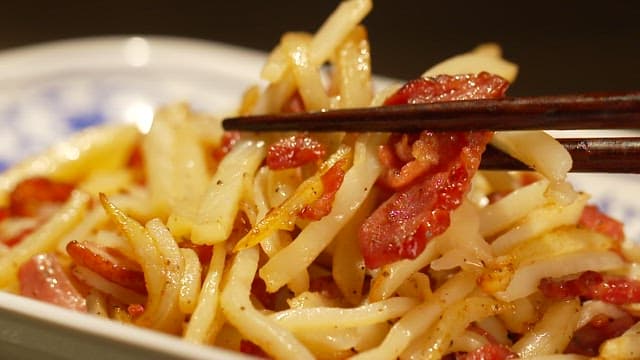 Chopsticks holding stir-fried shredded potatoes with smoked duck pieces