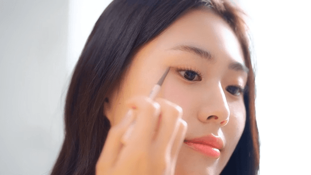 Woman applying eyeliner with concentration indoors