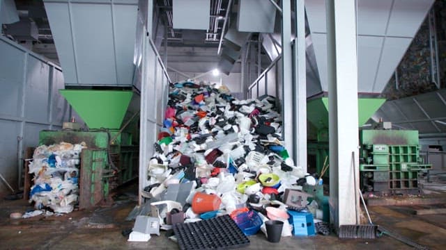 Plastic recycling facility with a large pile of mixed plastics on the conveyor belt