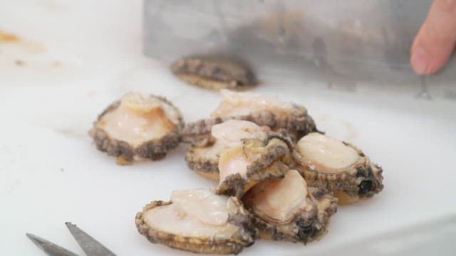 Cutting a abalone with a knife on a white cutting board