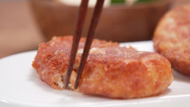 Picking up a fried fish cake with chopsticks on a white plate