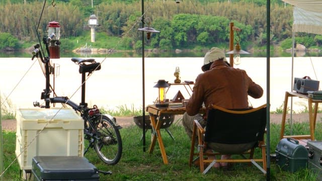 Person enjoying a peaceful campsite by the river with various camping equipment