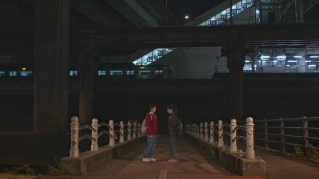 Two friends hugging on a dimly lit bridge at night under a railway station
