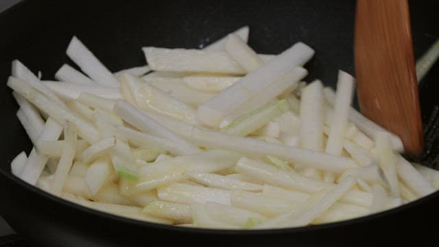 Shredded radish being stir-fried in a frying pan