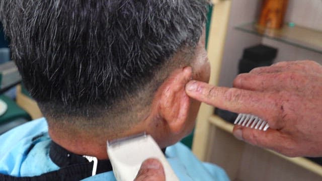 Barber trimming the hair behind a customer's ear in a salon with a clippers