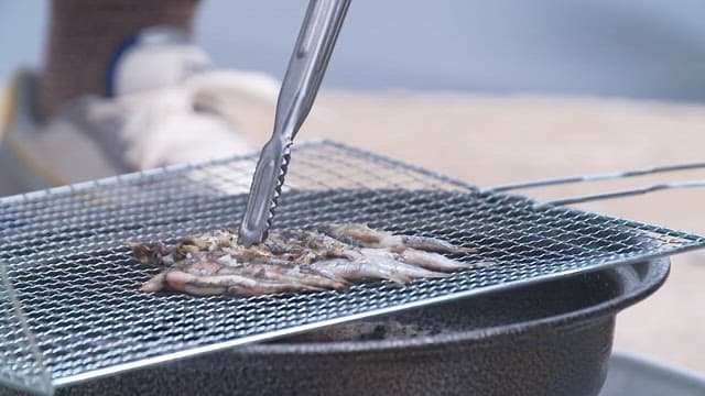Grilling anchovies on a small grill using tongs