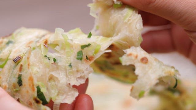 Hands tearing a green onion pancake