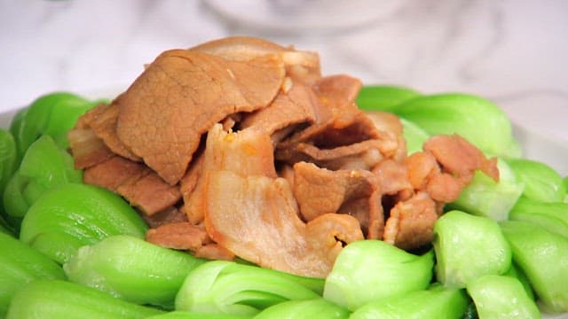 Sauce being poured over cooked meat and bok choy