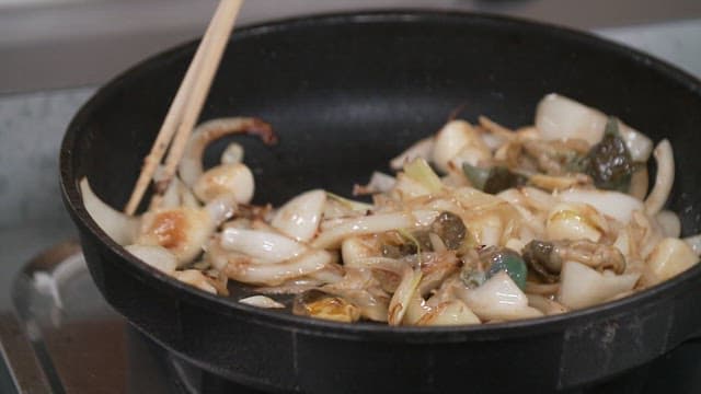 Stir-frying onions and abalones with chopsticks in a frying pan