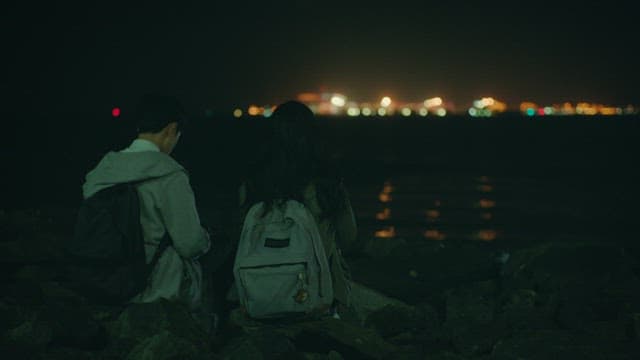 Two students sitting side by side on a beach with lights shining on them