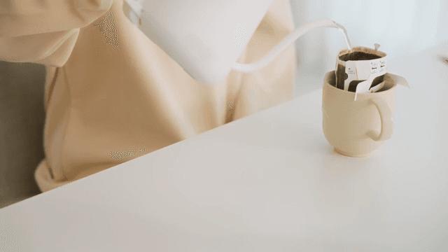 Woman pouring water into cup with coffee pot on table