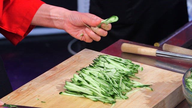 Cook lifting cucumbers cut on a wooden cutting board