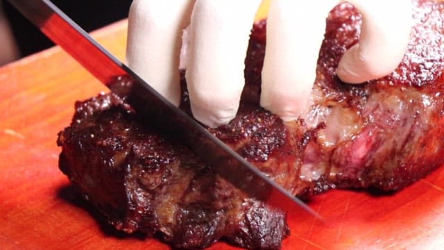 Hand Slicing a Well-Cooked Steak on a Cutting Board