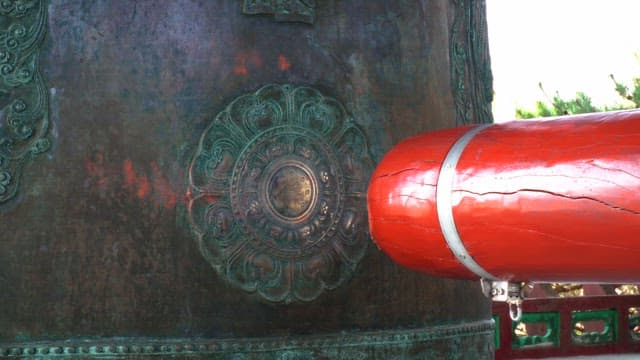 Ringing a large traditional bronze bell with a wooden hammer outdoors