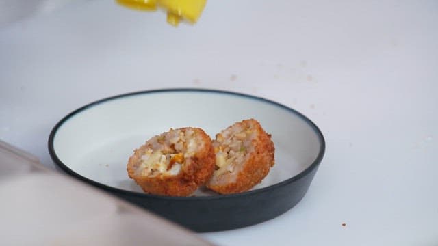 Ketchup being poured on fried arancini with bamboo shoots