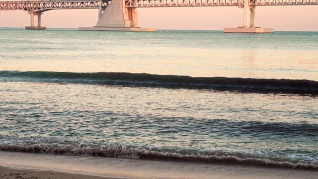 Waves Crashing Ashore Near a Large Bridge