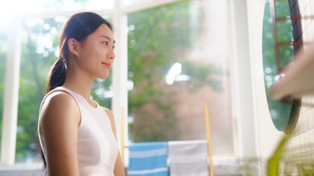 Woman applying skincare product by a sunny window