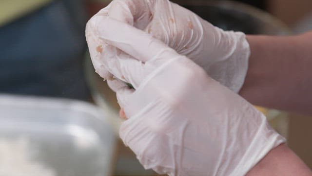 Gloved hands stuffing minced meat between perilla leaves