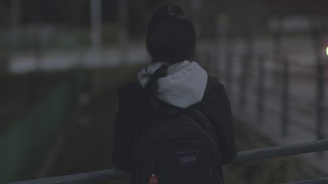Lone woman stands against a railing on a dark street at night