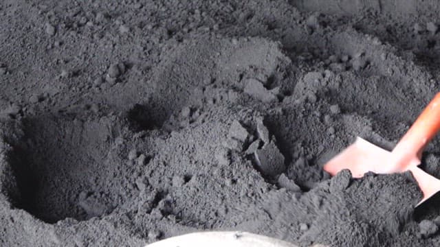 Scooping up black concrete powder with a shovel