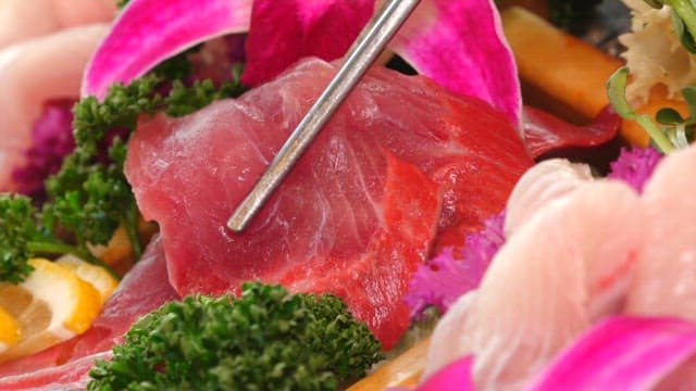 Yellow tail sashimi picked up with chopsticks