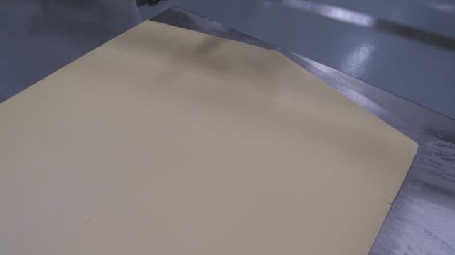 Worker in gloves cutting dough precisely with a ruler in an industrial kitchen setting