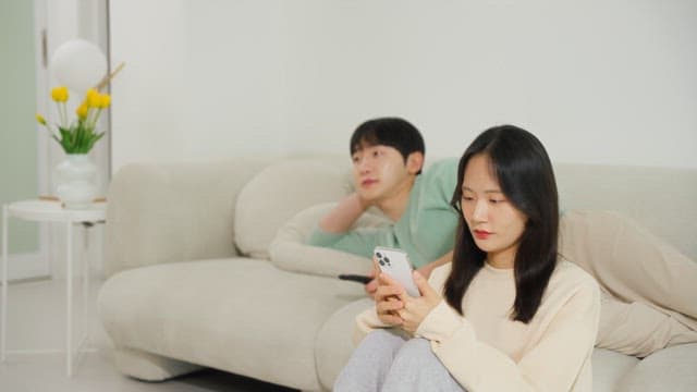 Using a smartphone and a man watching television on a sofa