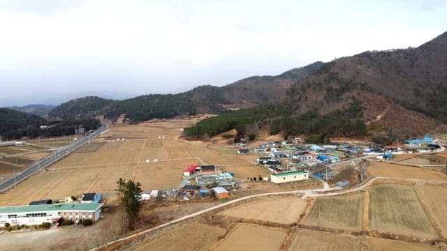 View of a rural village surrounded by fields and mountains on a cloudy day
