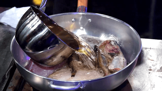 Pouring broth into a pot containing various types of fish
