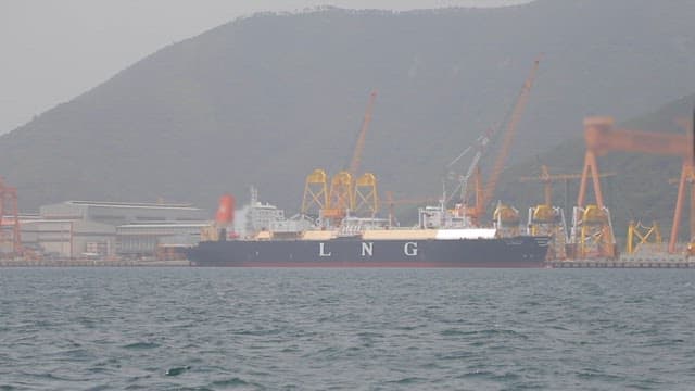 LNG ship docked at an industrial harbor with cargo cranes