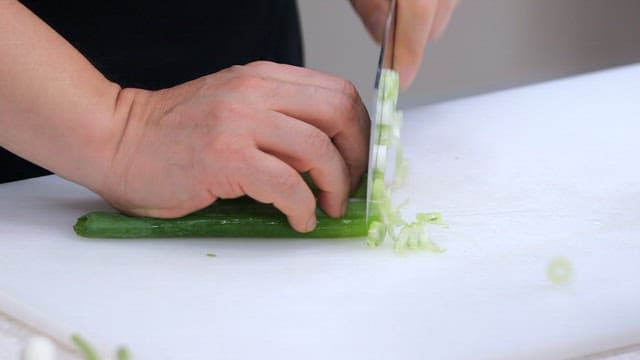 Chopping fresh green onions with a knife on a white cutting board