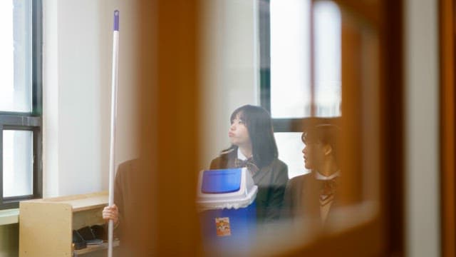 Students in school uniforms holding cleaning tools