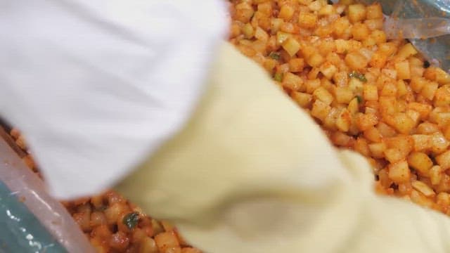 Mixing spicy diced radish kimchi in a stainless steel bowl.