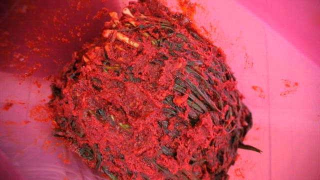 Well-seasoned green onion kimchi in a kimchi container on a wooden table