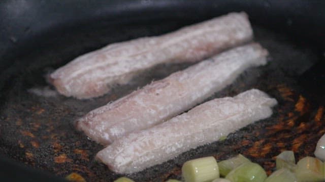 Frying green onions and hairtail in oil in a frying pan