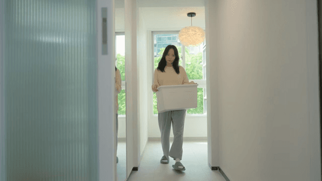Woman walking through house with bright interior holding storage box