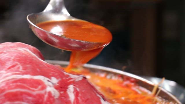 Broth of stew being poured over raw beef in a pot